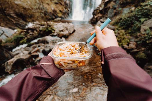 Enjoying a pasta meal by a scenic waterfall with a focus on outdoor adventure.