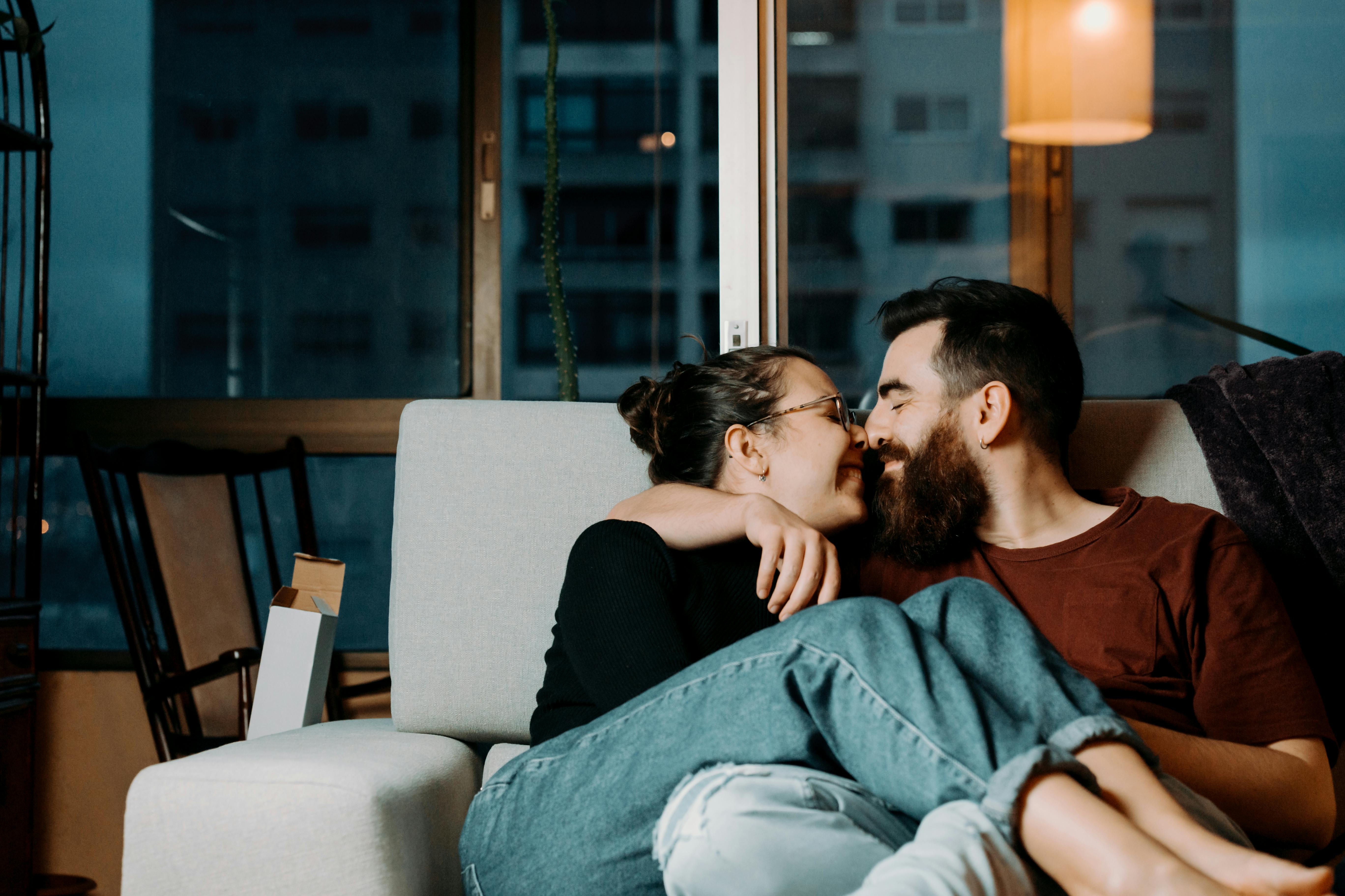 A couple sharing an affectionate moment indoors, nestled on a sofa during the evening.