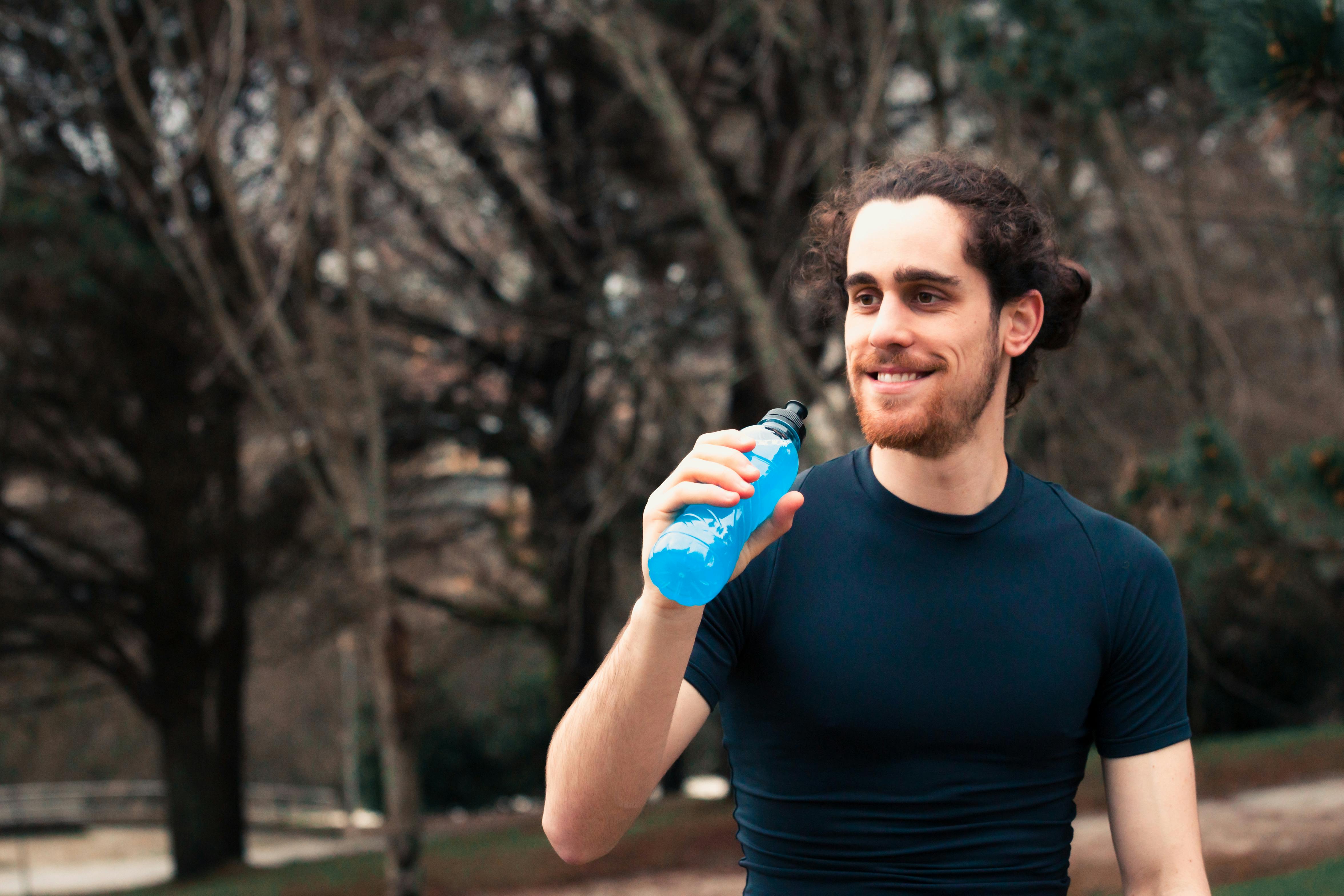 bearded young man in black t shirt holding blue bottle