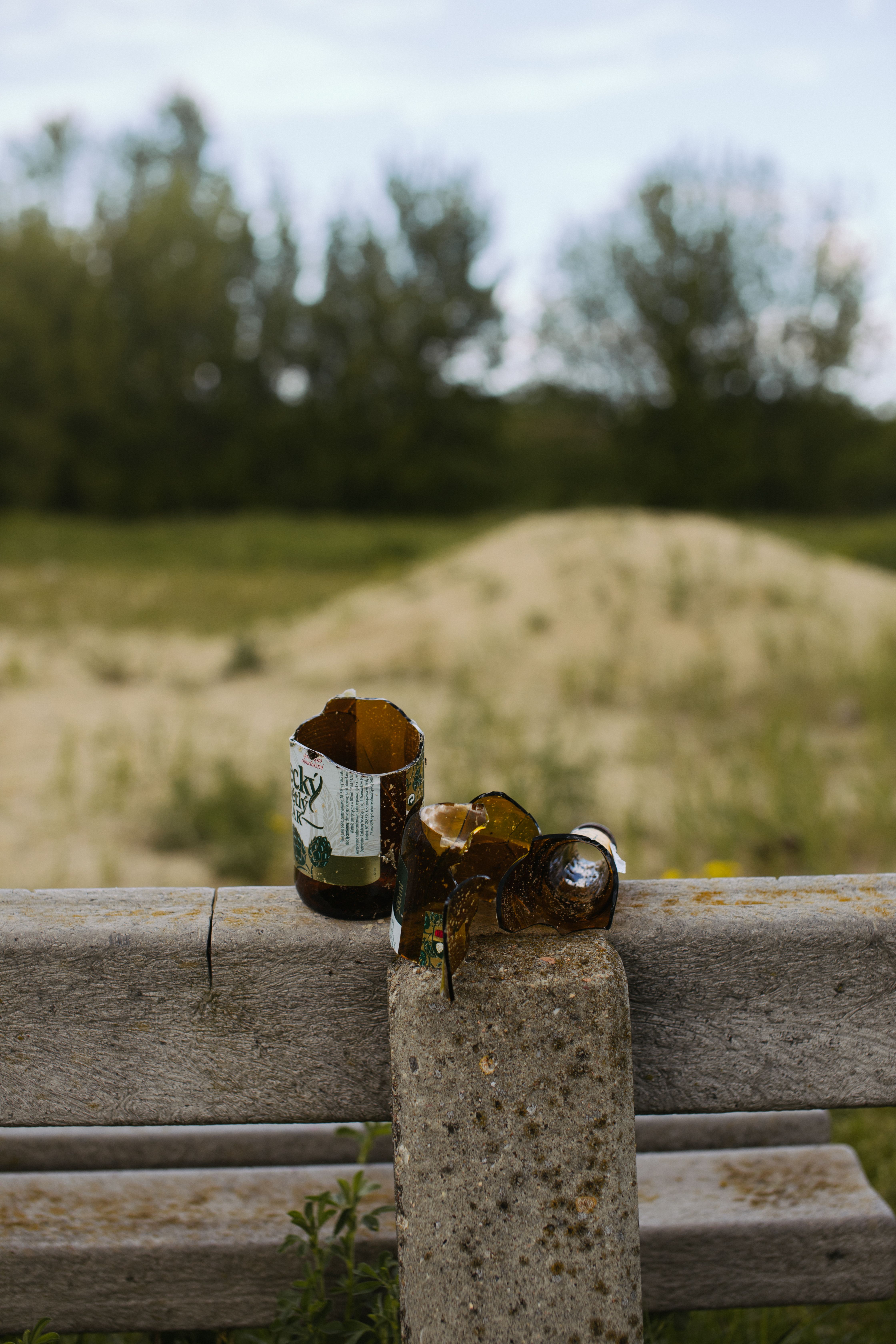 A shattered glass bottle on a concrete fence in an outdoor field.