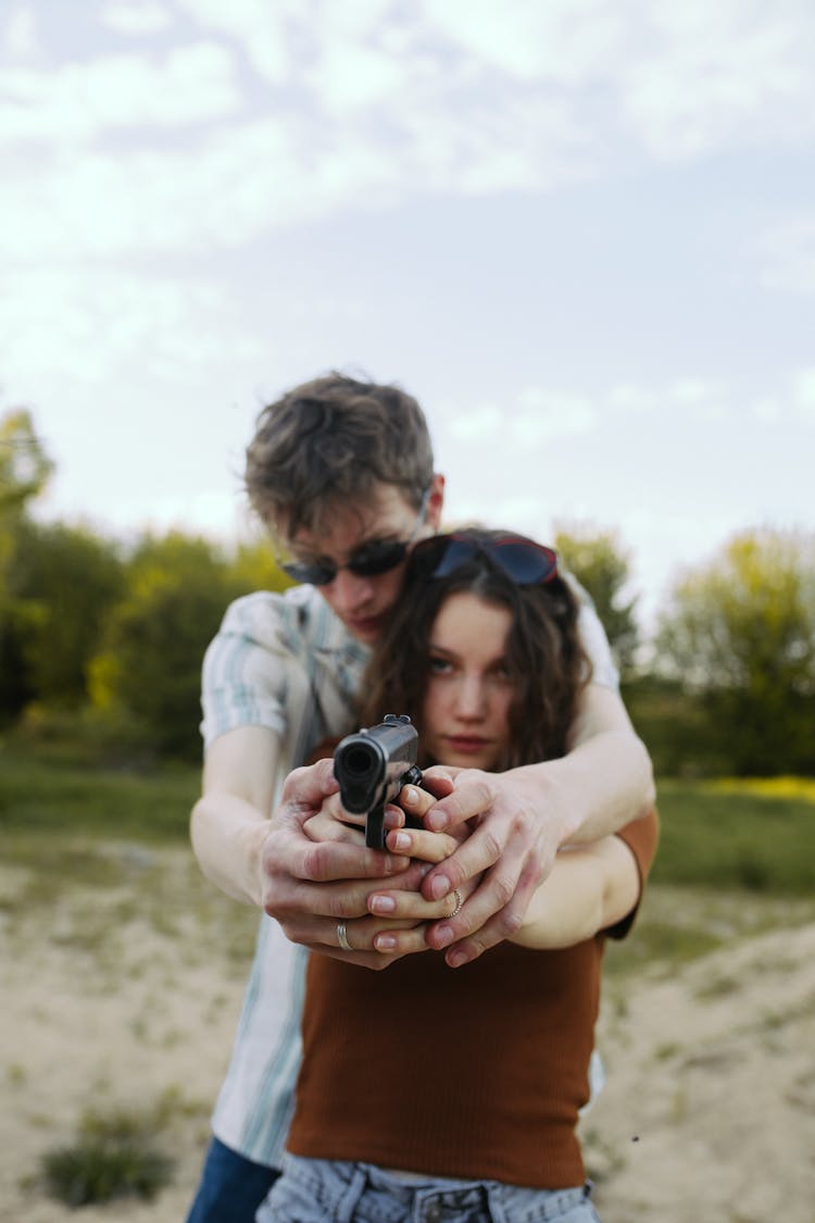 A Man Teaching A Woman How To Hold A Firearm