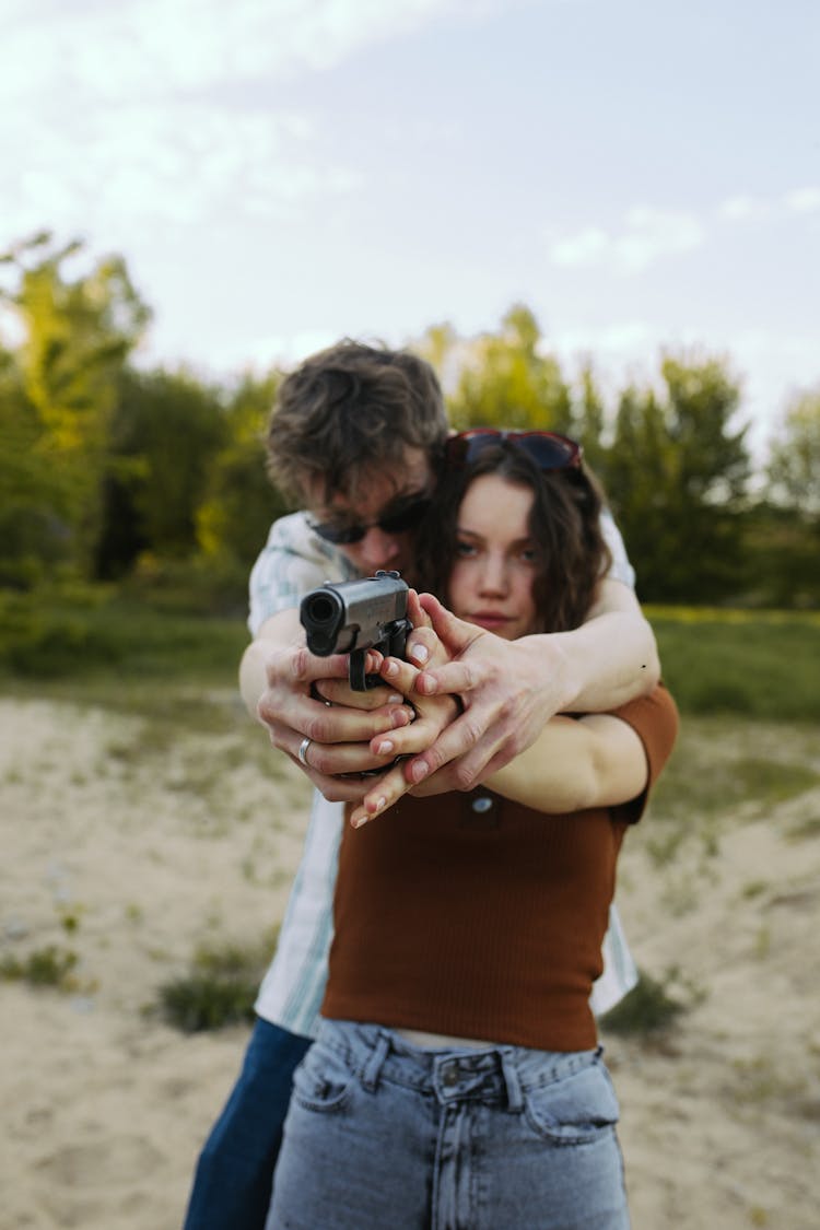 A Man Teaching A Woman How To Hold A Firearm