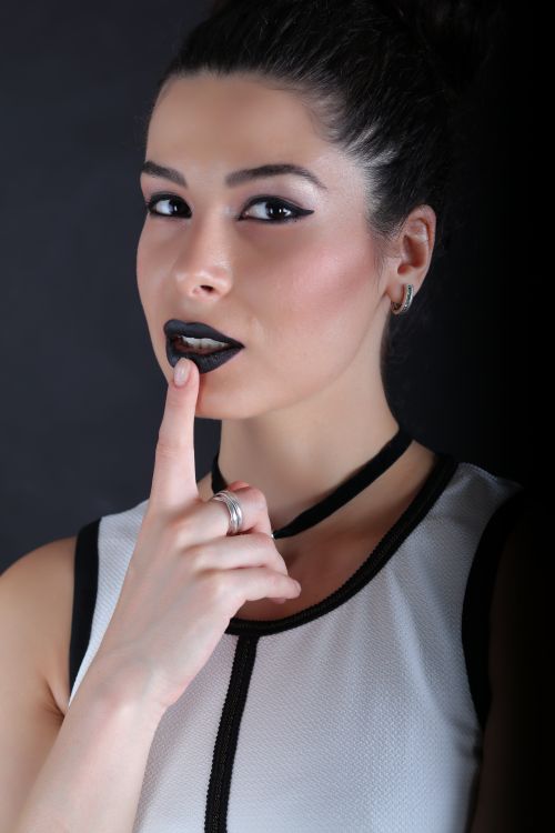 Free Close-up portrait of a stylish woman with striking black lipstick against a dark background. Stock Photo