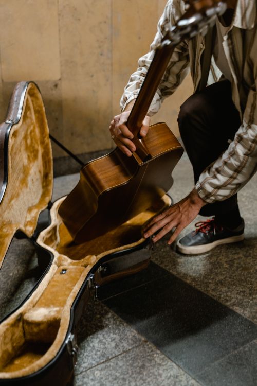 Free A street performer carefully packs his guitar into a case on a city sidewalk. Stock Photo