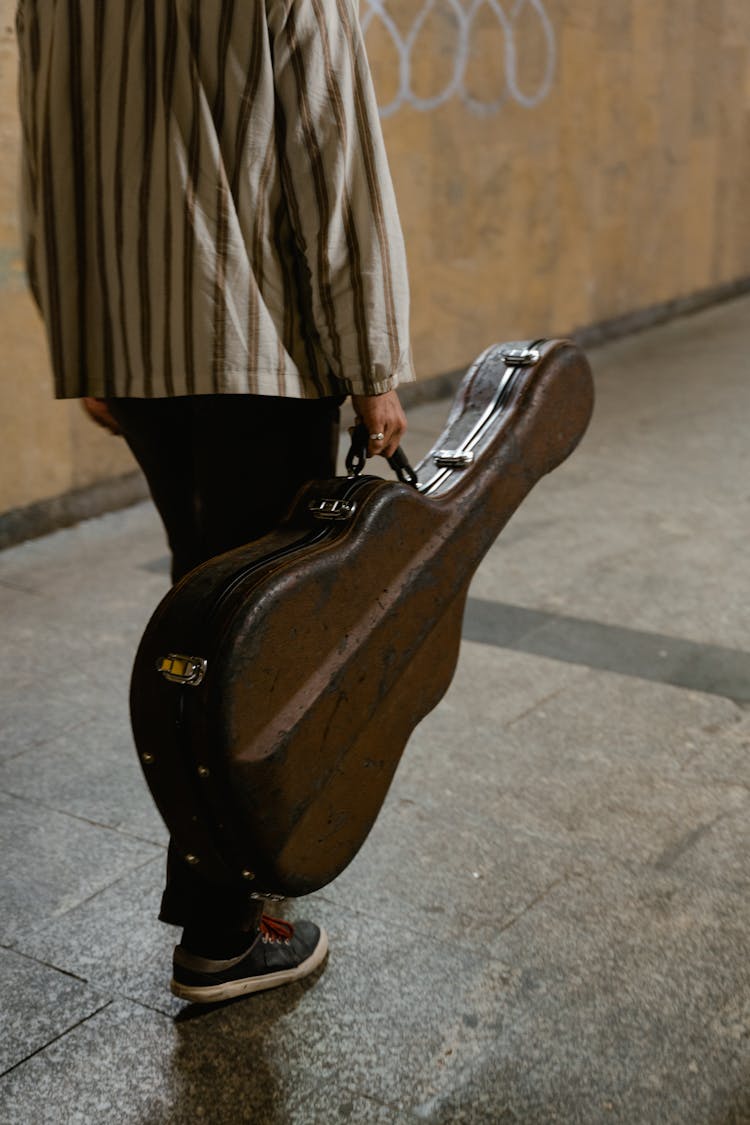 Person In Brown Shirt Holding Brown Guitar Case