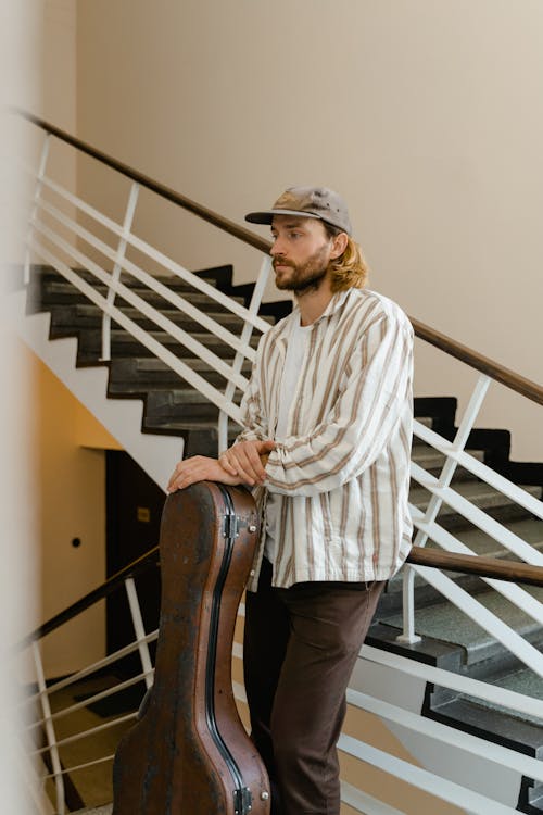Man in White and Brown Striped Dress Shirt and Black Pants Standing on Staircase