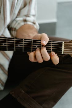 Detailed close-up of a man playing an acoustic guitar indoors, focused on hand placement.