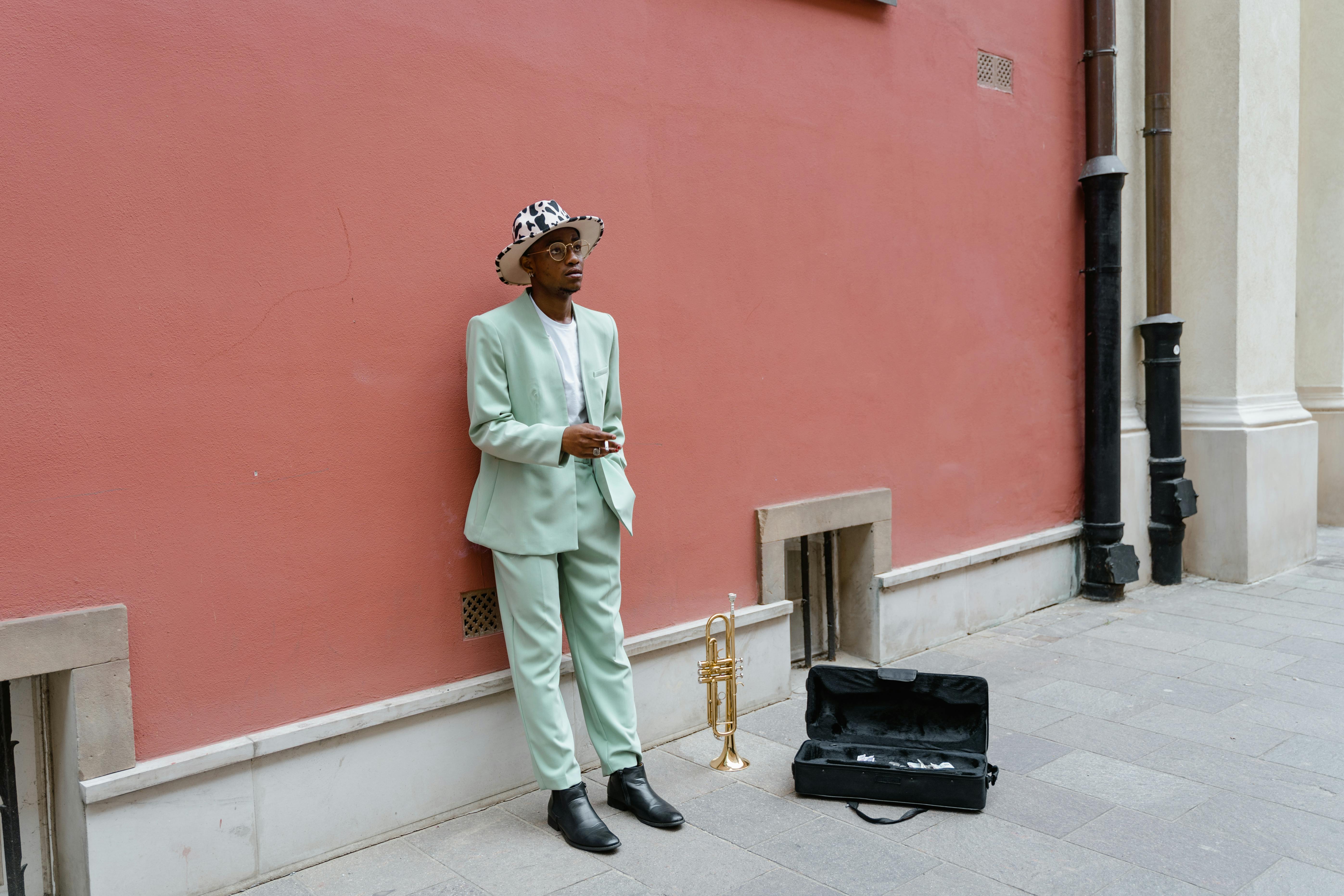 Free A trendy musician in a pastel suit busking with a trumpet against a red wall. Stock Photo
