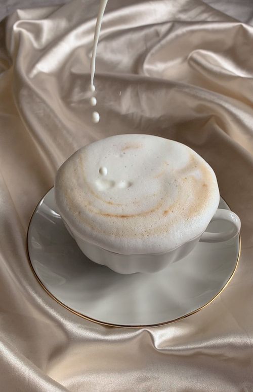 Free Delicate cappuccino topped with foam as milk pours, set against luxurious satin fabric. Stock Photo