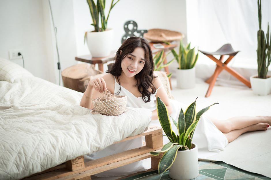 Elegant bedroom scene with a smiling woman surrounded by potted plants and stylish decor.