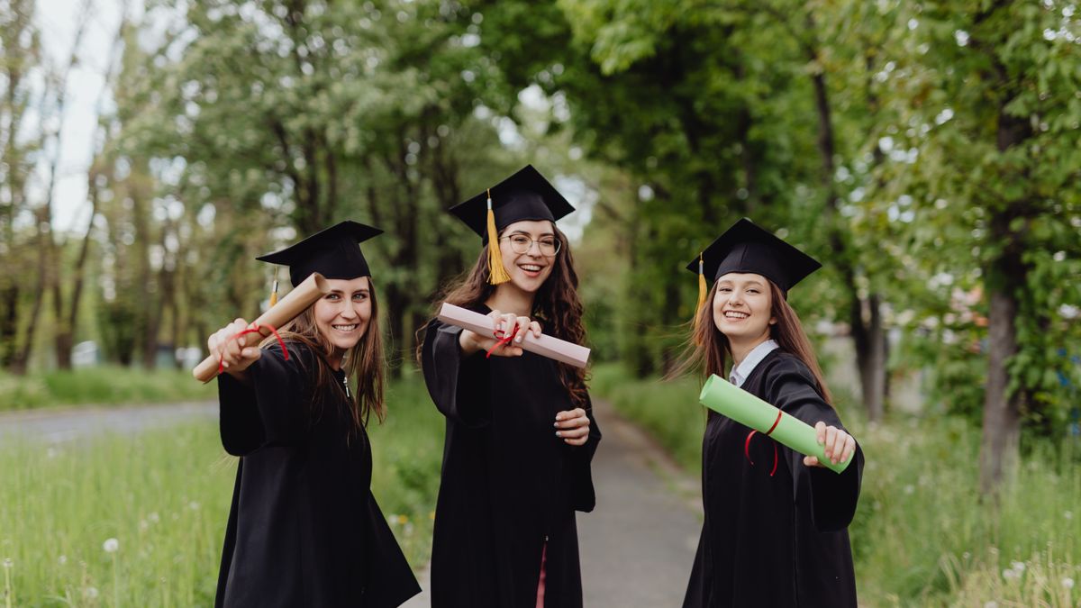 Jovens formandas de beca e capelo seguram seus diplomas ao ar livre