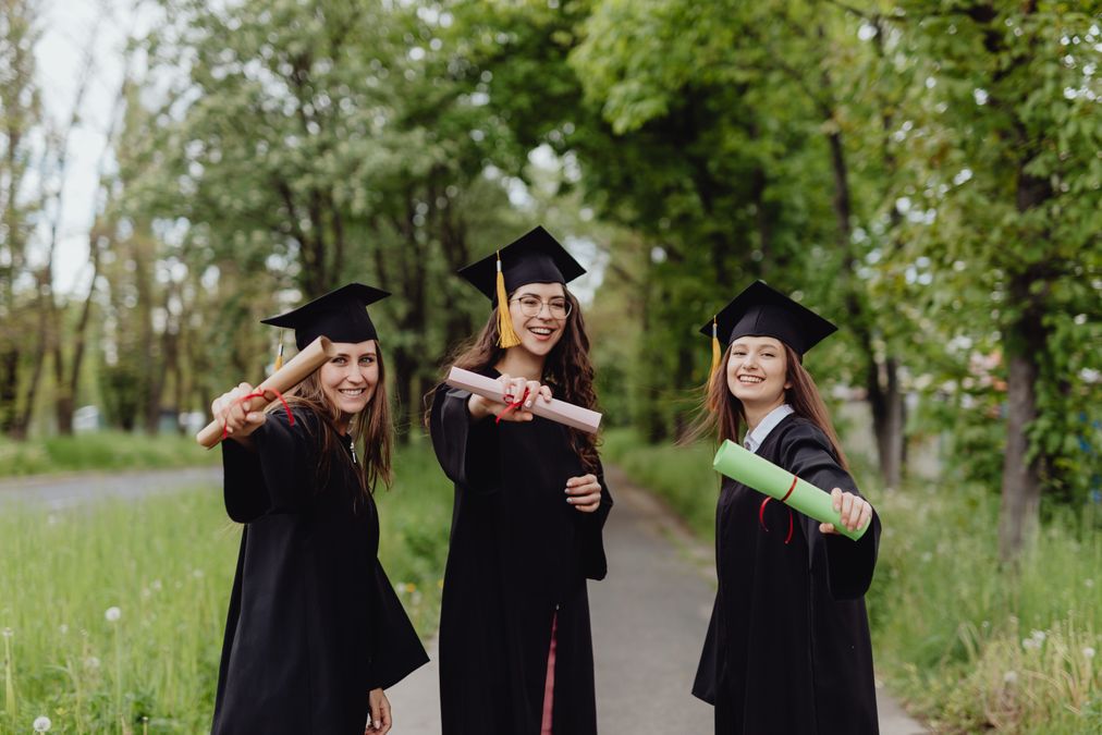 Jovens formandas de beca e capelo seguram seus diplomas ao ar livre