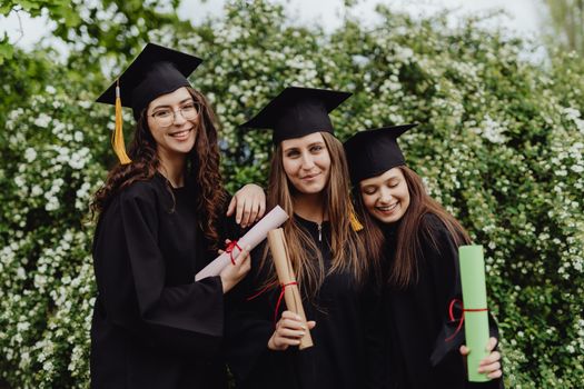 Group of smiling young women graduates posing with diplomas outdoors.