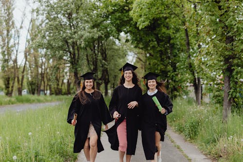 Free Women in Black Academic Dress Walking on the Pathway Stock Photo