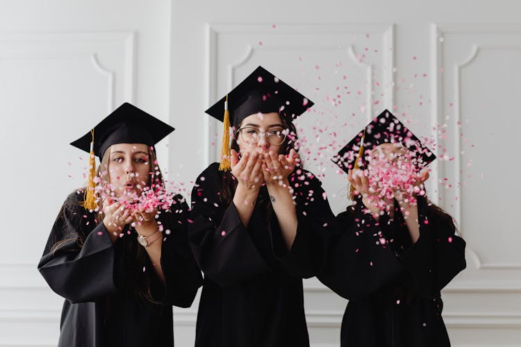 Women Wearing Graduation Caps Blowing Confetti