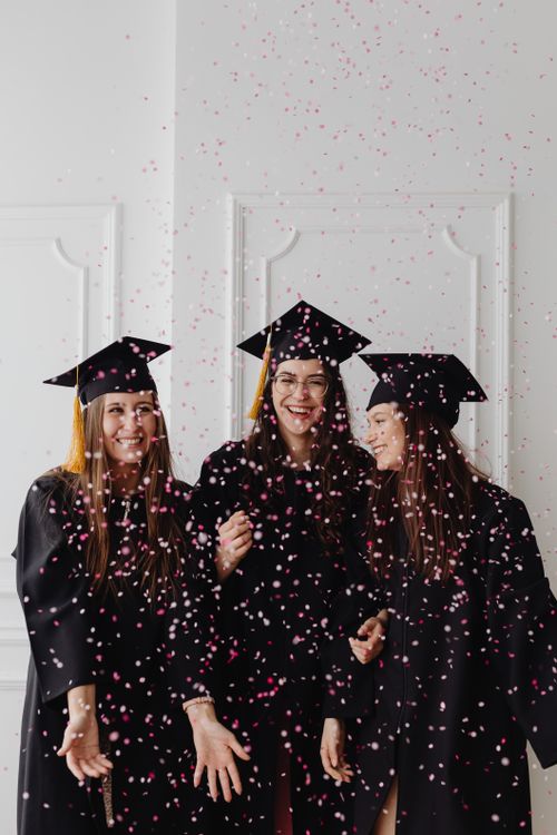 Free Three women graduates joyfully celebrate with confetti indoors, showcasing excitement and success. Stock Photo
