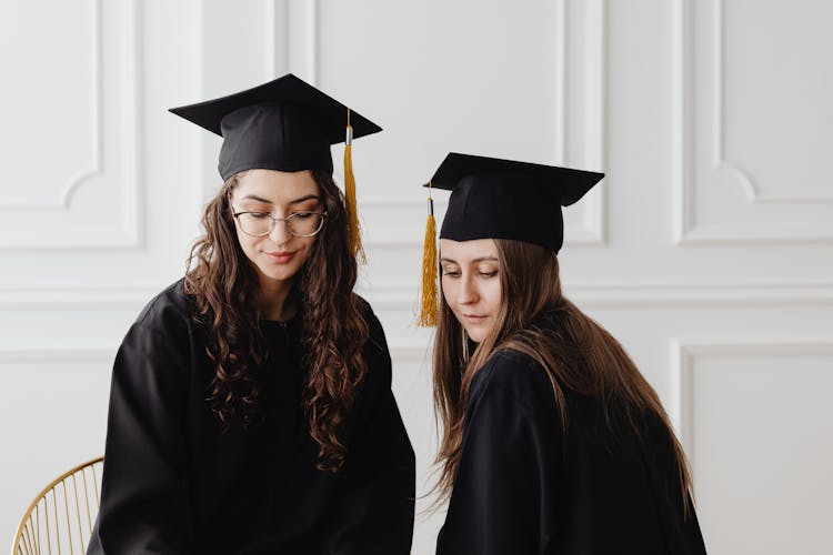 Two Women In Graduation Gowns And Caps