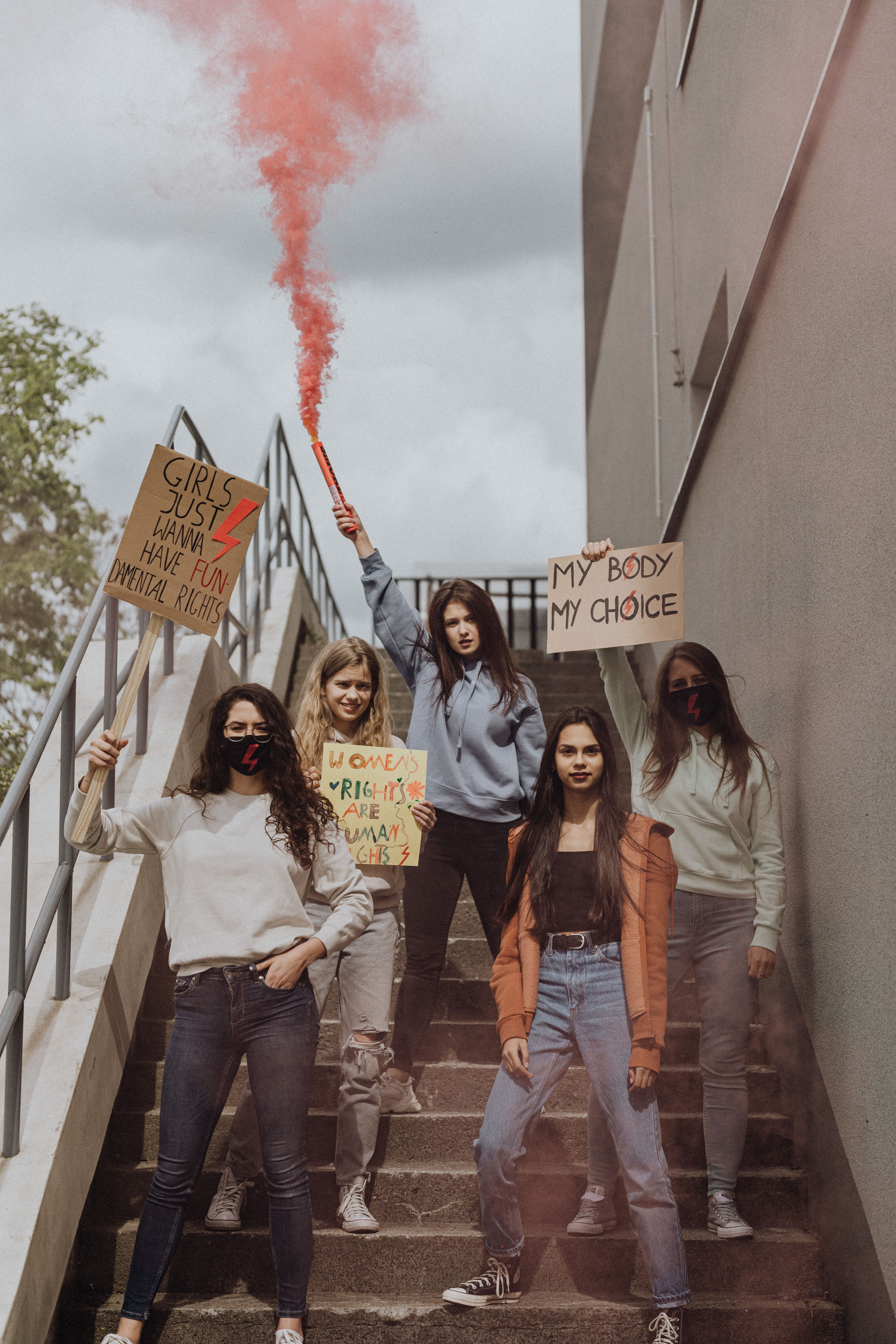 Group of women on stairs holding placards and smoke flare, advocating for gender rights.