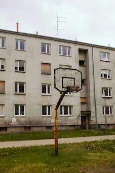 A derelict basketball hoop stands in front of an abandoned building.