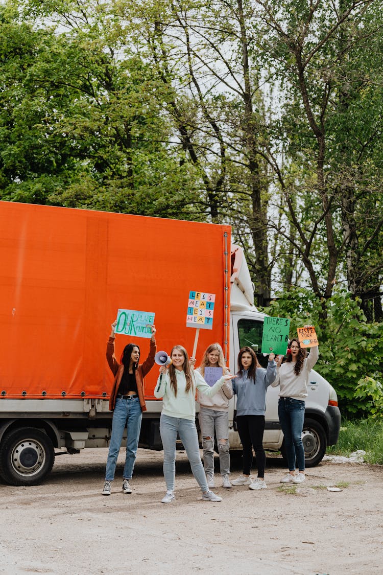 A Group Of Women Standing Near The Truck While Holding Placards And Megaphone