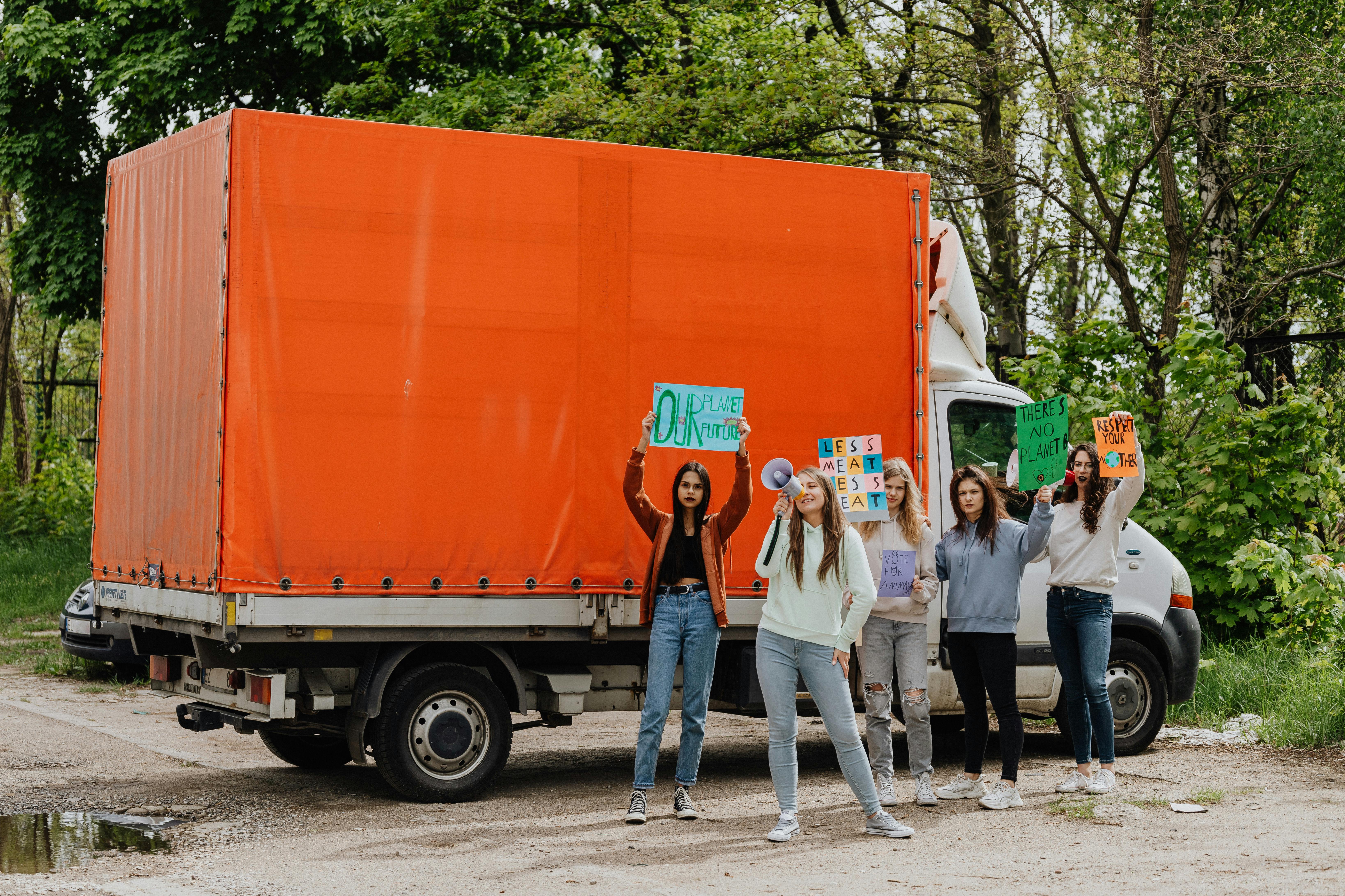 Group of young women protesting outdoors with signs and banners by a truck.