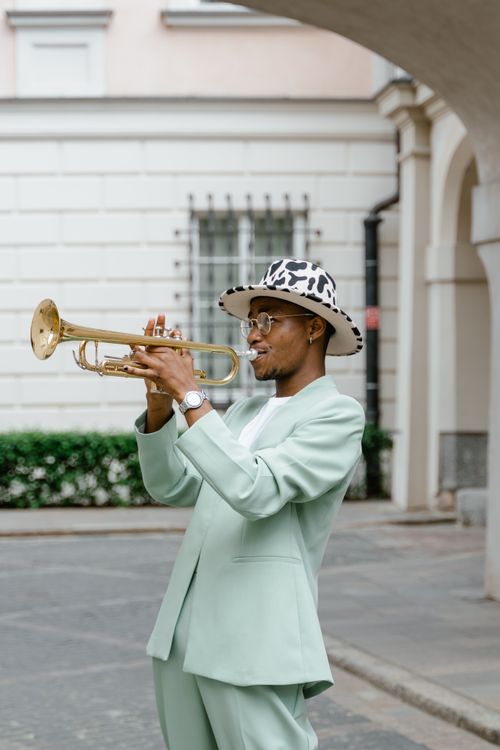 Free African American man in stylish suit and hat playing trumpet on city street. Stock Photo