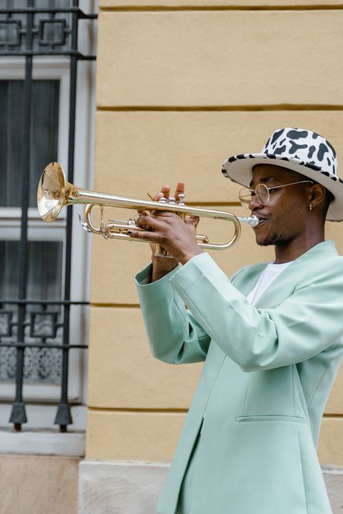 Free Stylish street musician performs with a trumpet, wearing a striking suit and hat. Stock Photo
