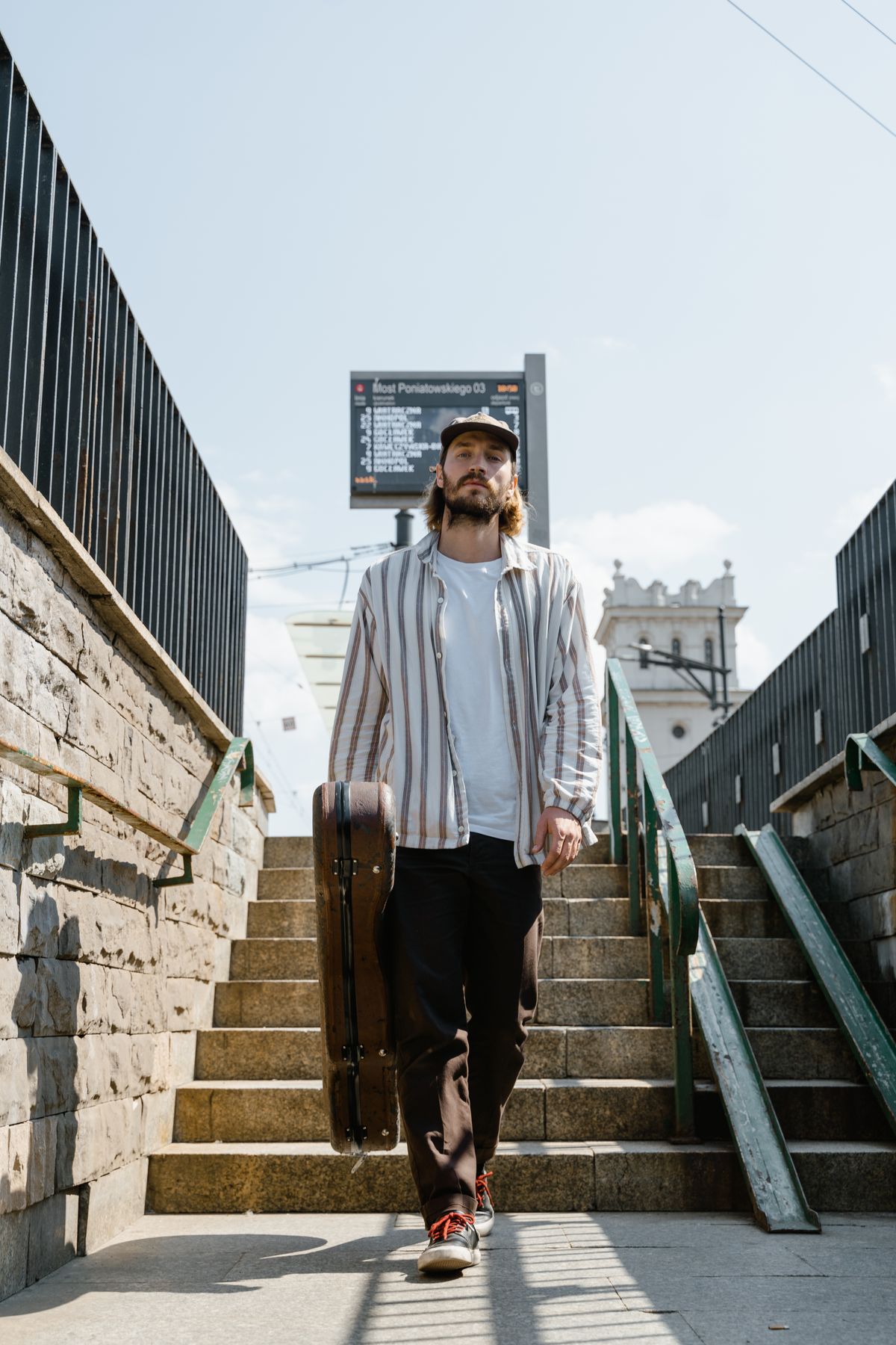 A musician carrying a guitar case down a flight of steps in an urban setting