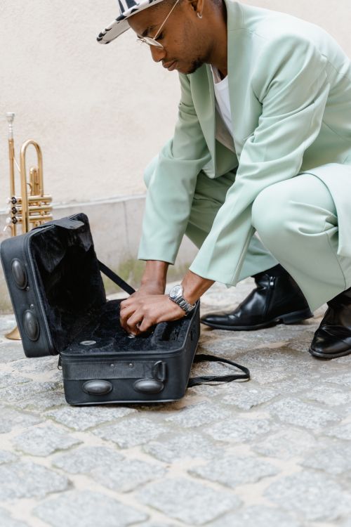 Free A street performer organizes his instrument case outdoors, preparing to play the trumpet in a city setting. Stock Photo