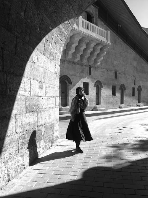 Monochrome Photo of an Elderly Woman in an Arched Hallway 