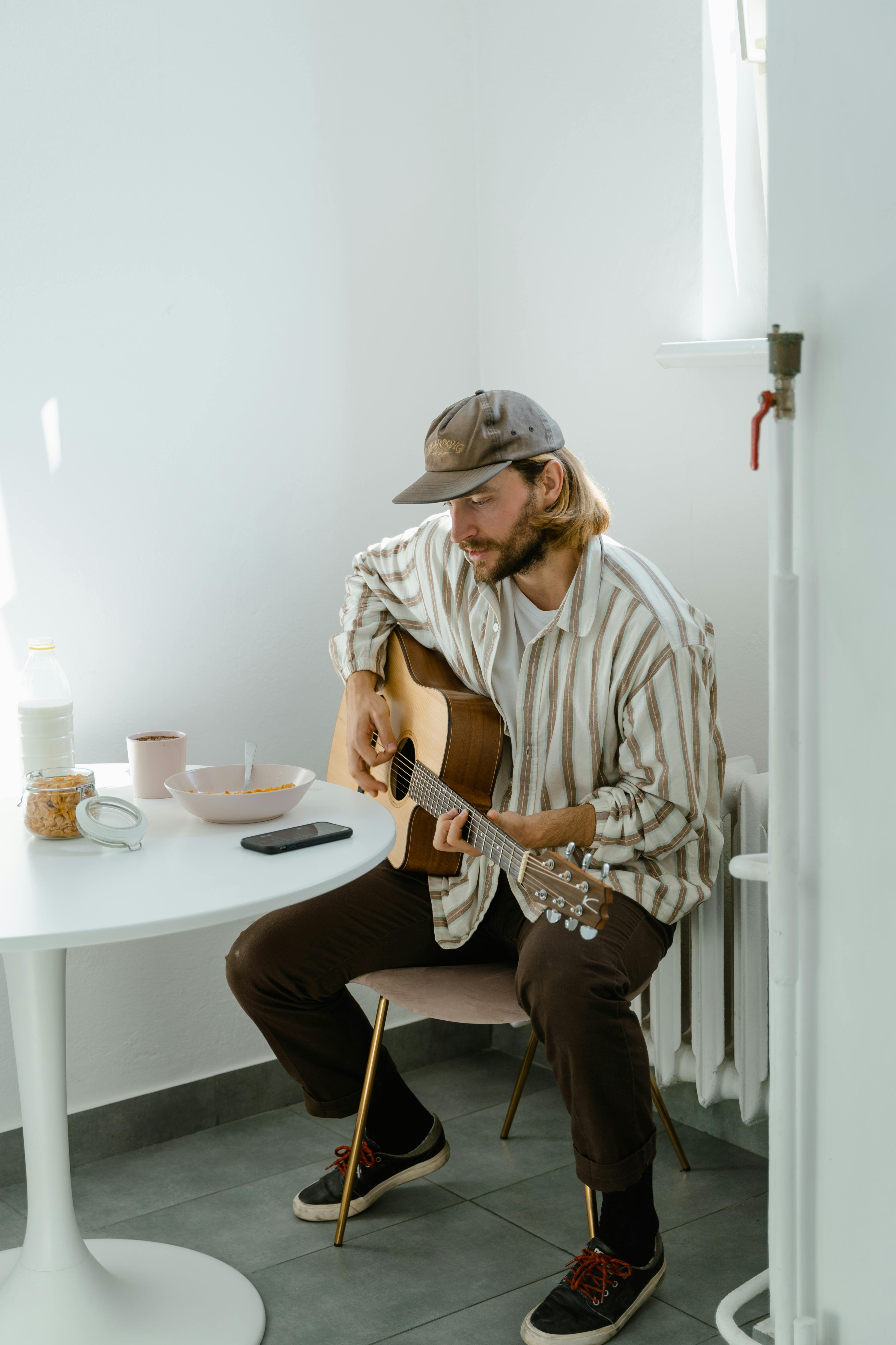Adult male playing acoustic guitar in a minimalist dining room, focusing on music.