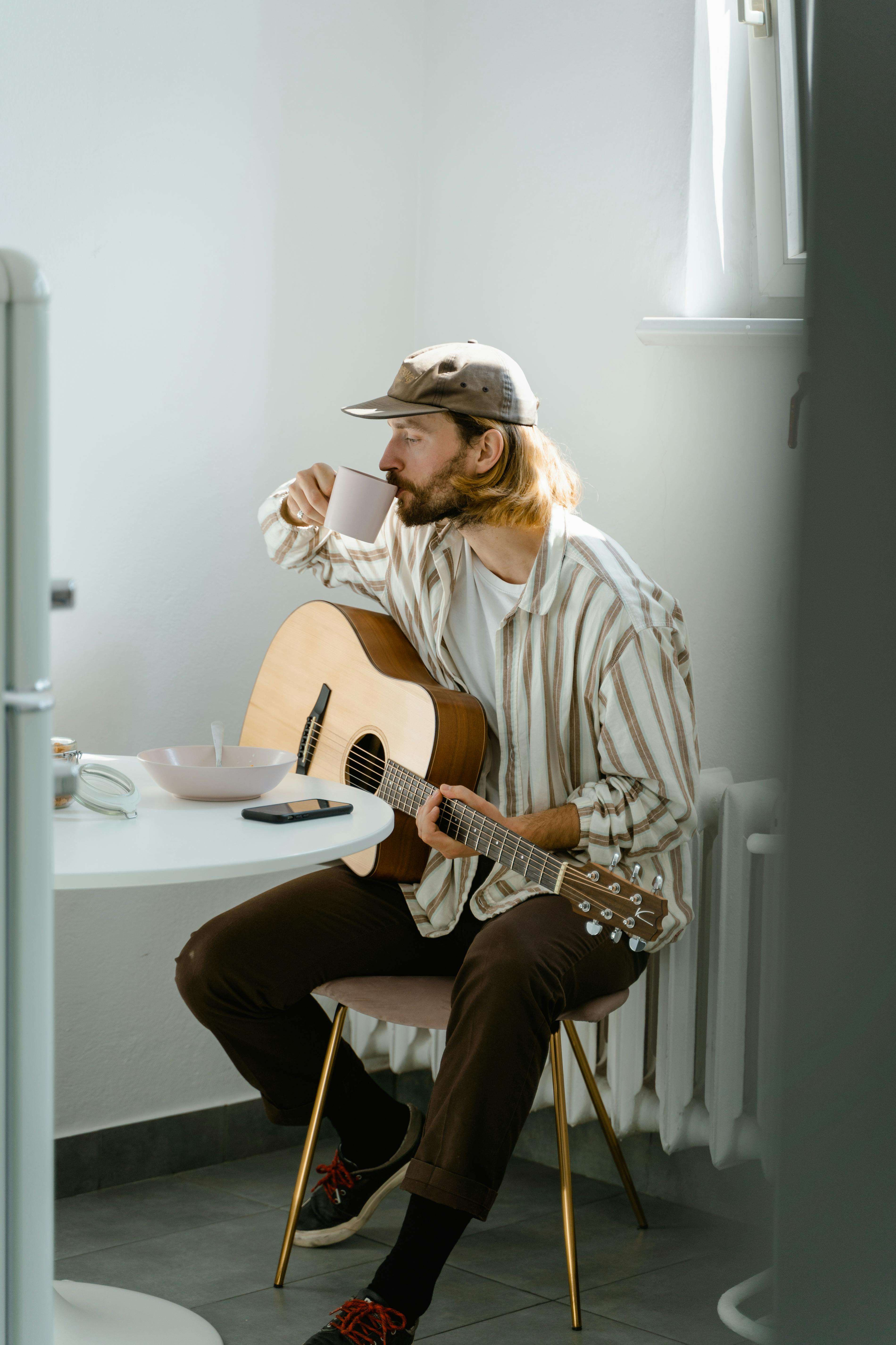 A man with a guitar enjoys coffee in a cozy indoor setting.