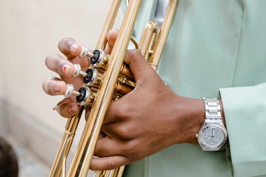 A detailed view of a musician's hands playing a trumpet outdoors with a focus on the instrument and wristwatch.