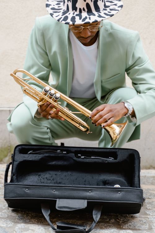 Free Street musician in a stylish outfit, playing a brass trumpet outdoors with an open instrument case. Stock Photo