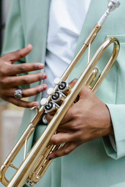 Free A person's hands playing a trumpet, dressed in a stylish green outfit during the daytime. Stock Photo