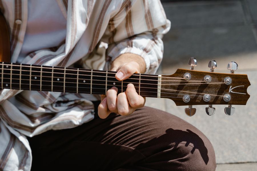 Close view of fingers fretting an acoustic guitar in warm sunlight