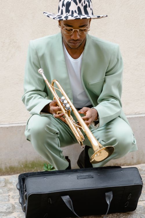 Free A stylish musician in a green suit preparing a trumpet for street performance. Stock Photo