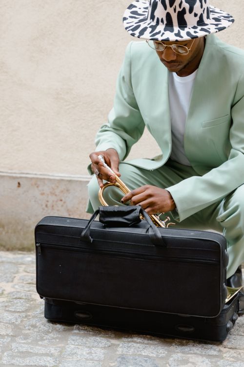 Free A fashionably dressed musician prepares his trumpet on a street. Stock Photo
