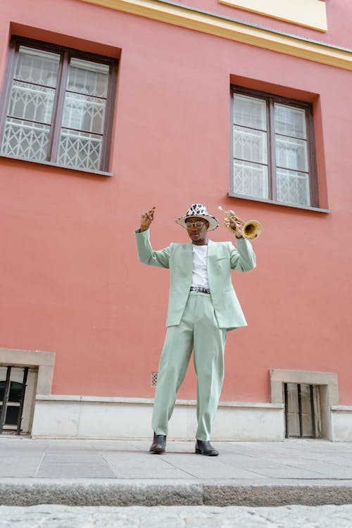 Man in Teal Suit Standing Near Pink Concrete Building