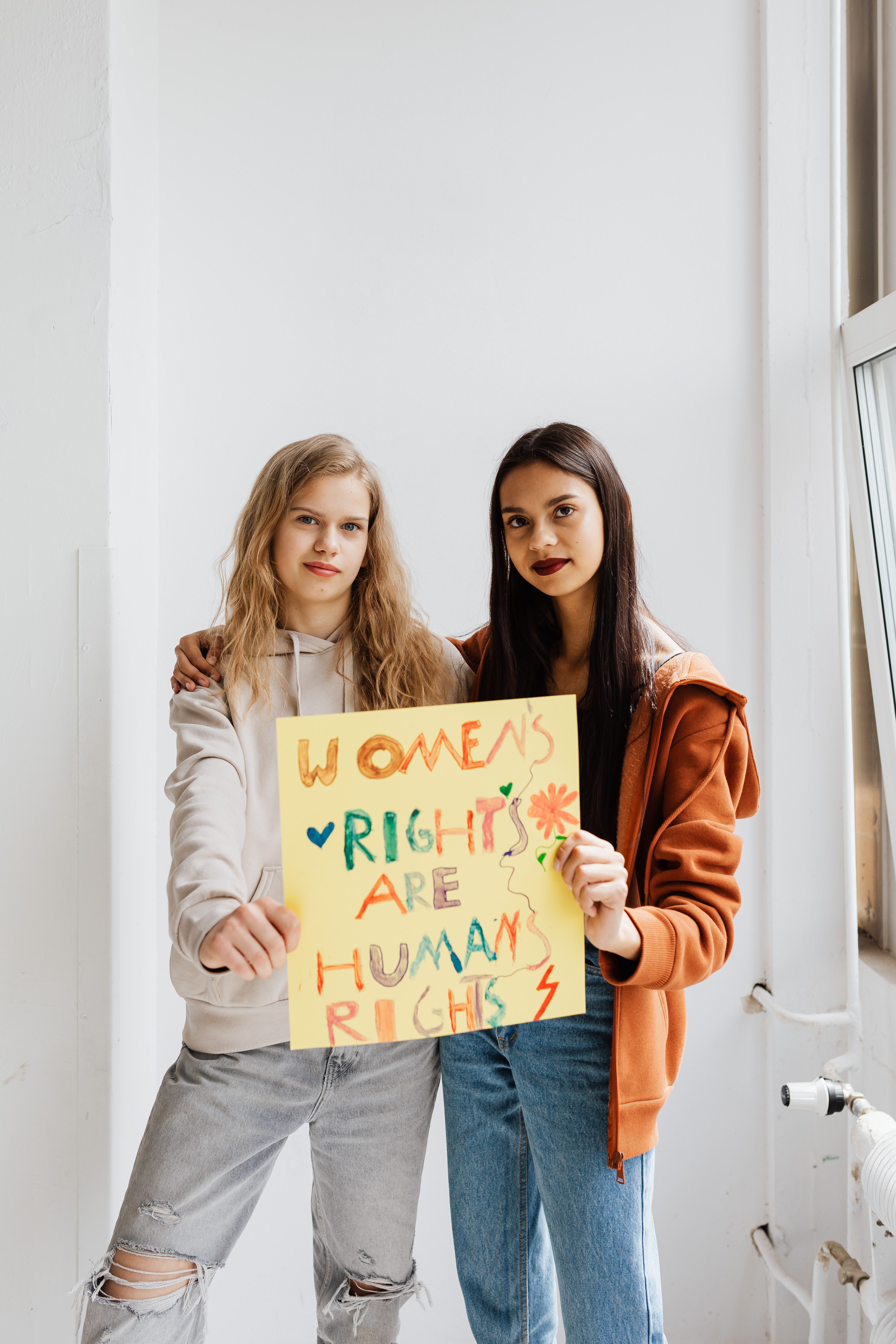 Two women holding a colorful sign advocating for women's rights indoors.