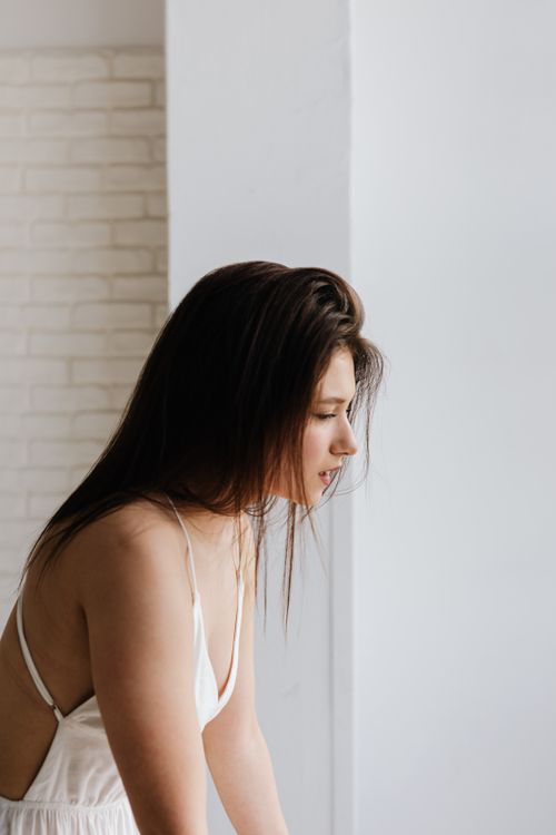 Free Side profile of a woman in a white dress gazing out of a window. Stock Photo