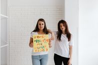 2 Women Standing Beside White Wall