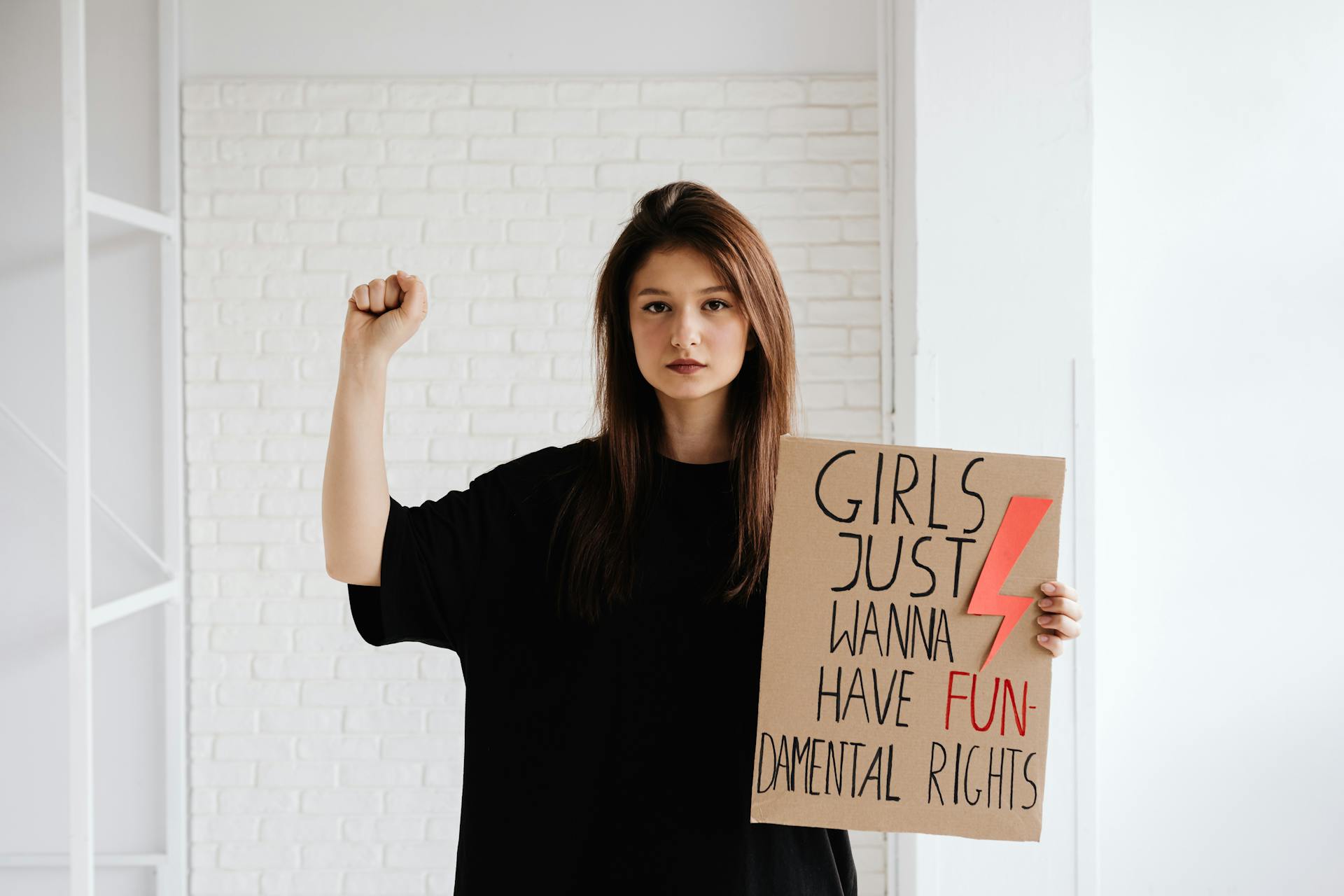 A young woman holds a protest sign advocating for fundamental women's rights indoors.