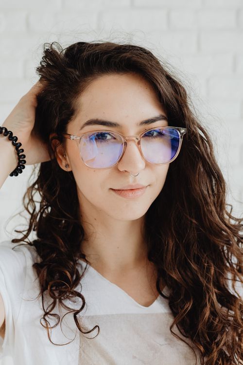 Free Elegant portrait of a young woman with curly hair and eyeglasses, posing indoors. Stock Photo