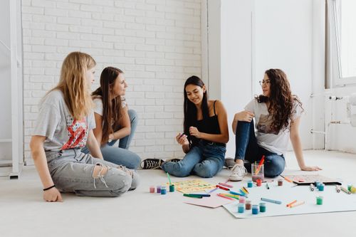 Free Four young women sitting indoors, working on a creative art project with paints and markers. Stock Photo