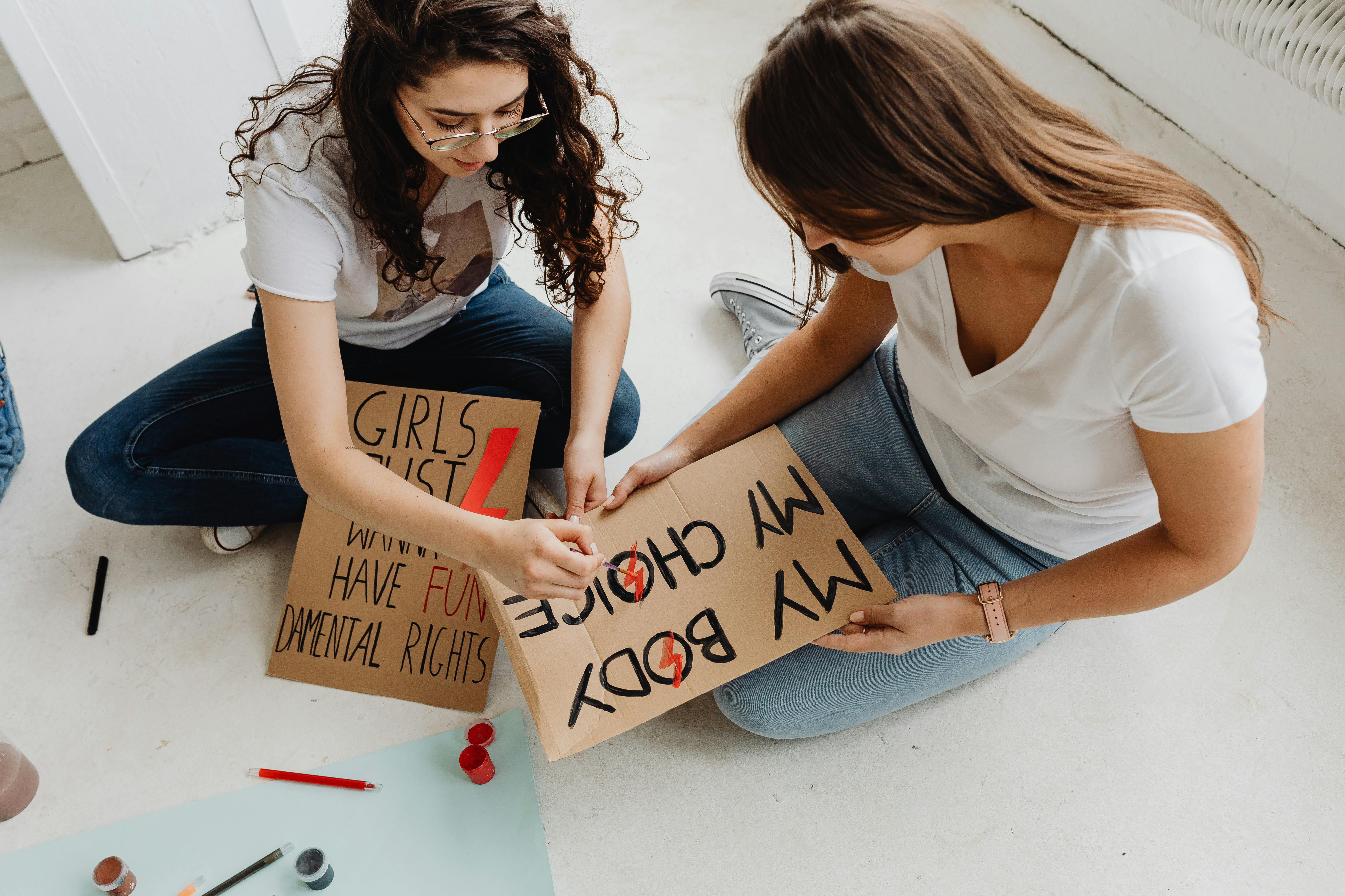 women sitting on the floor while writing on the placard