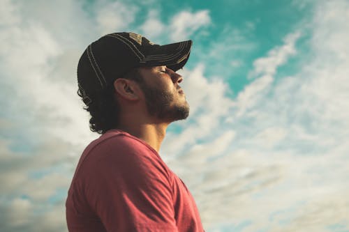 Gratis Pria Mengenakan Topi Hitam Dengan Mata Tertutup Di Bawah Langit Berawan Foto Stok