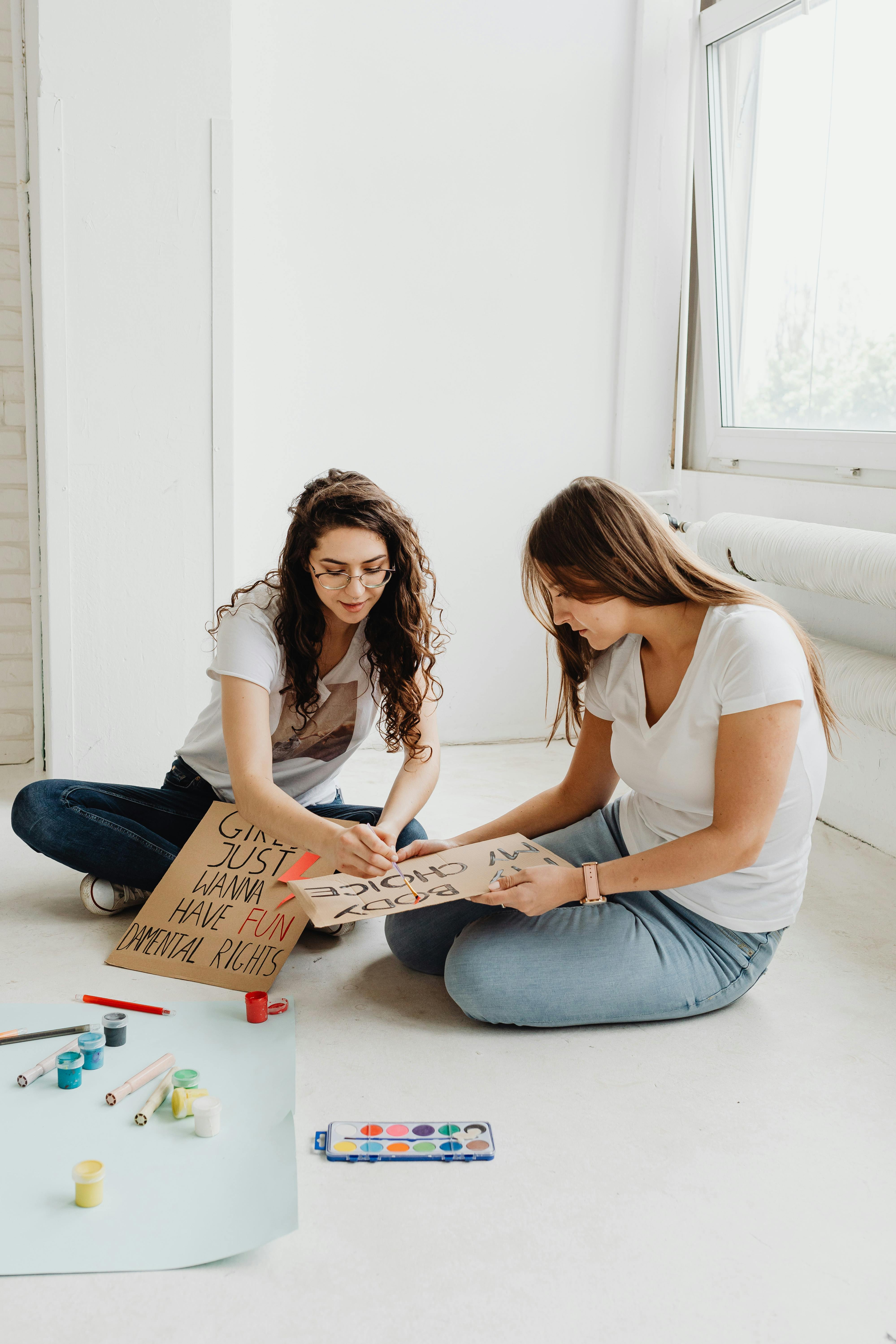 women sitting on the floor while writing on the placards