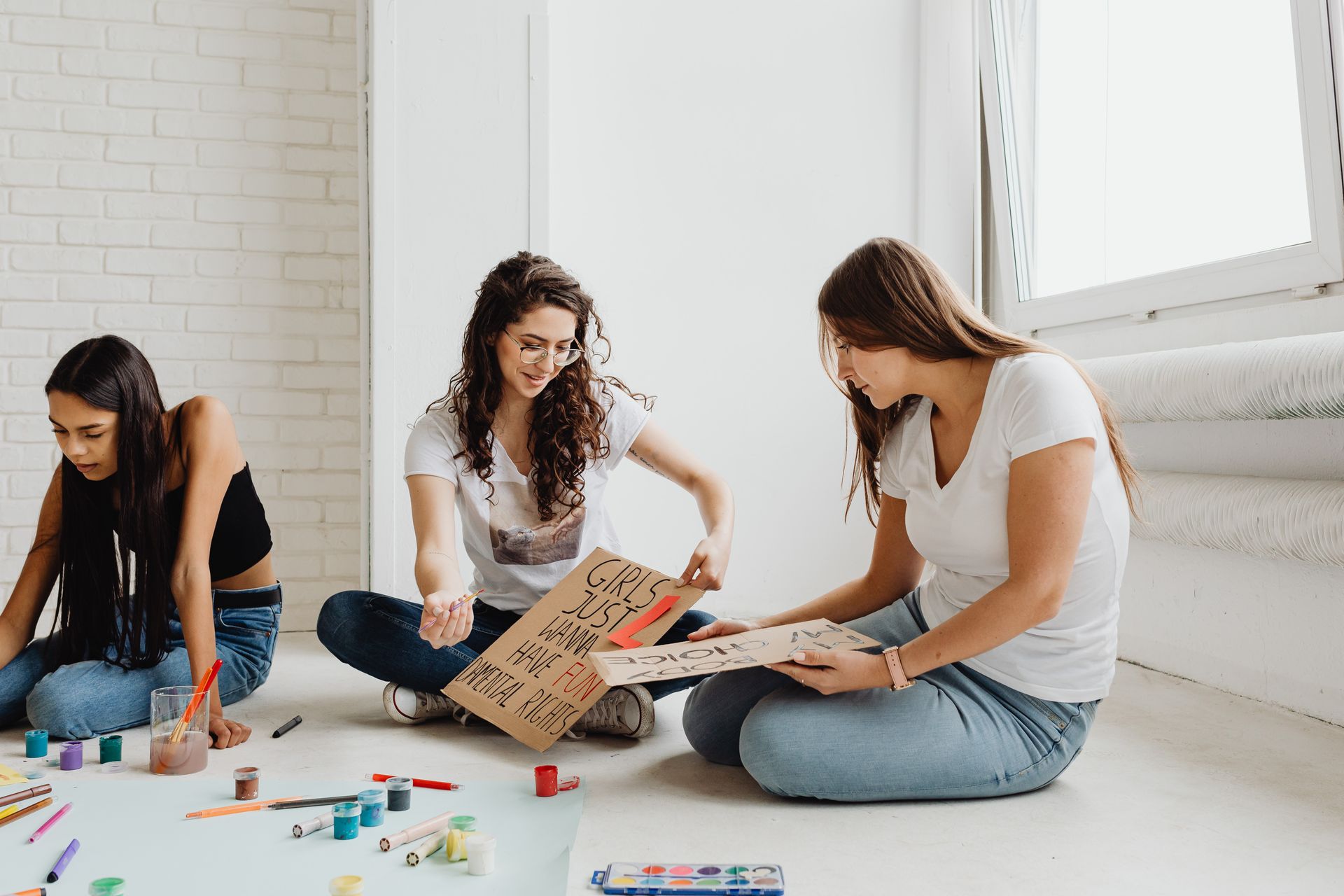 Three women crafting protest signs indoors, focusing on art and activism.