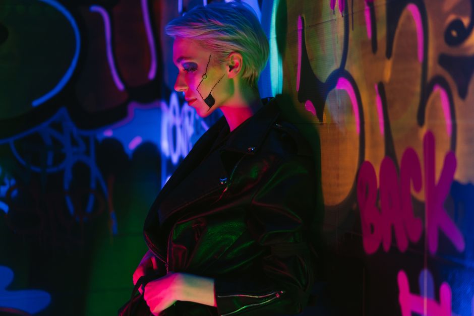 A woman in a cyberpunk style poses against neon graffiti, embodying a futuristic and edgy vibe.